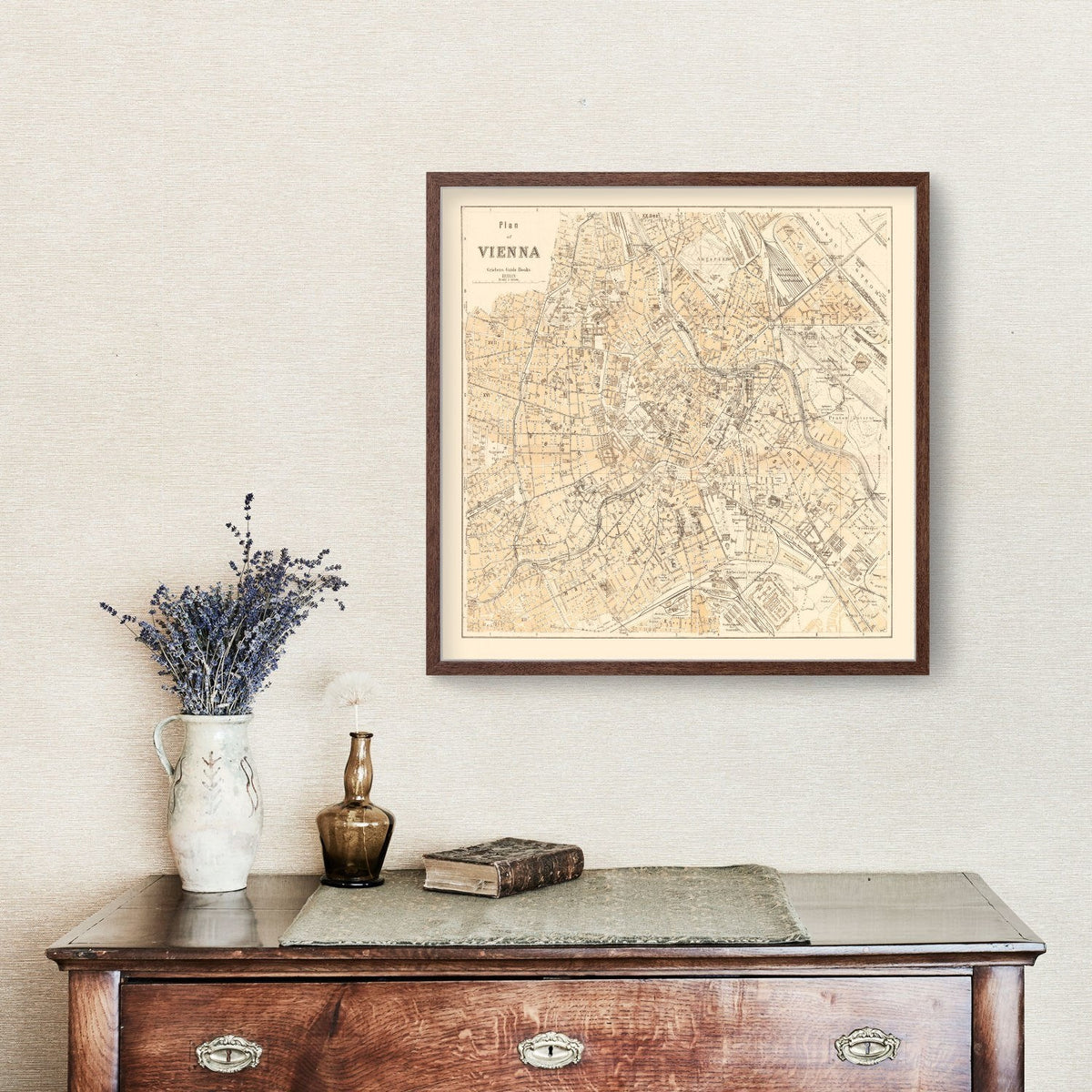 Framed Vienna map above an antique-style wooden chest with flowers and books