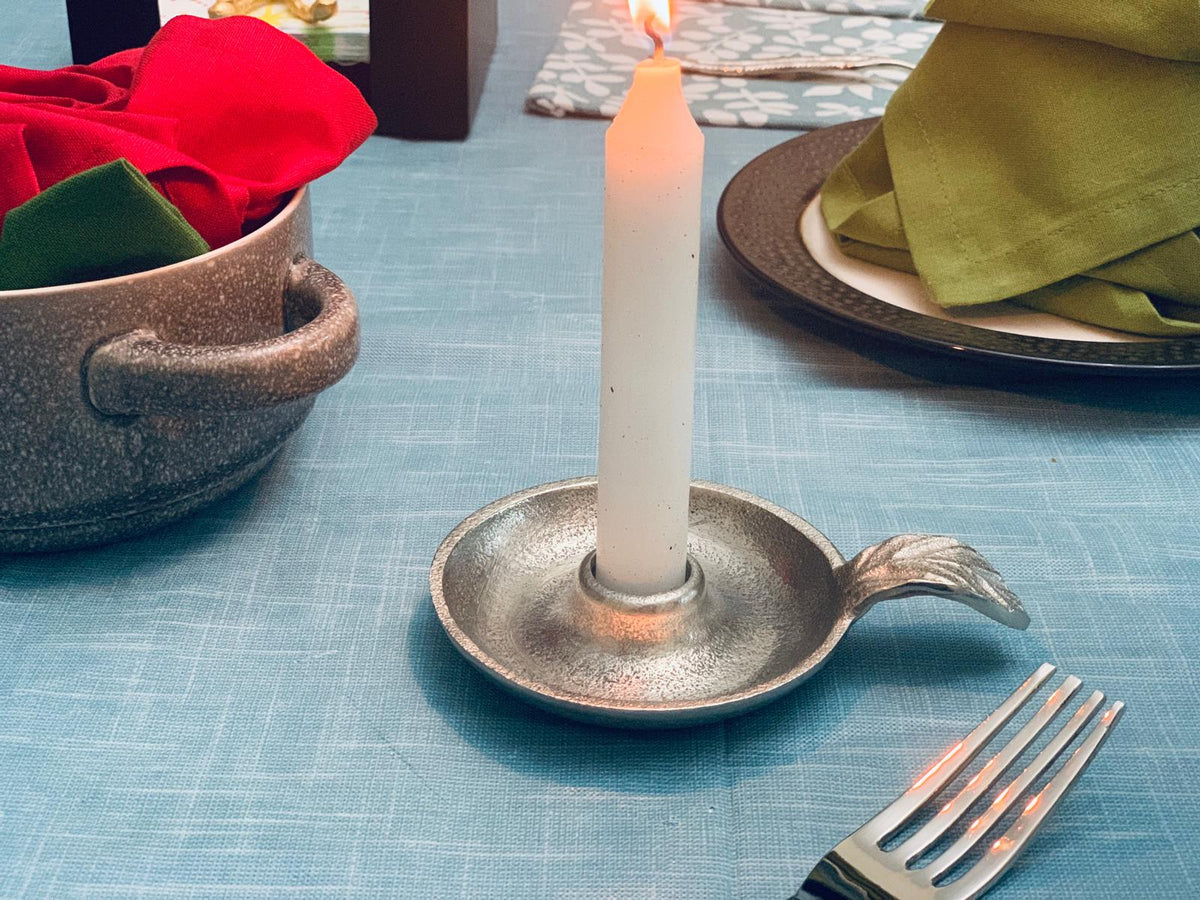 Silver taper candle holder with a lit candle on a blue dining table