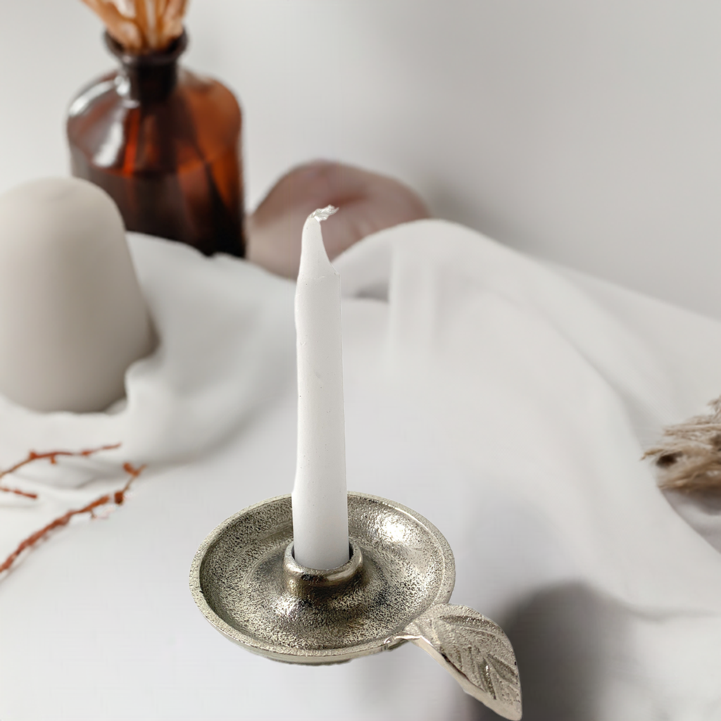 Silver leaf-handle candle holder styled with white fabric and an amber bottle