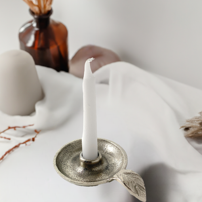 Silver leaf-handle candle holder styled with white fabric and an amber bottle