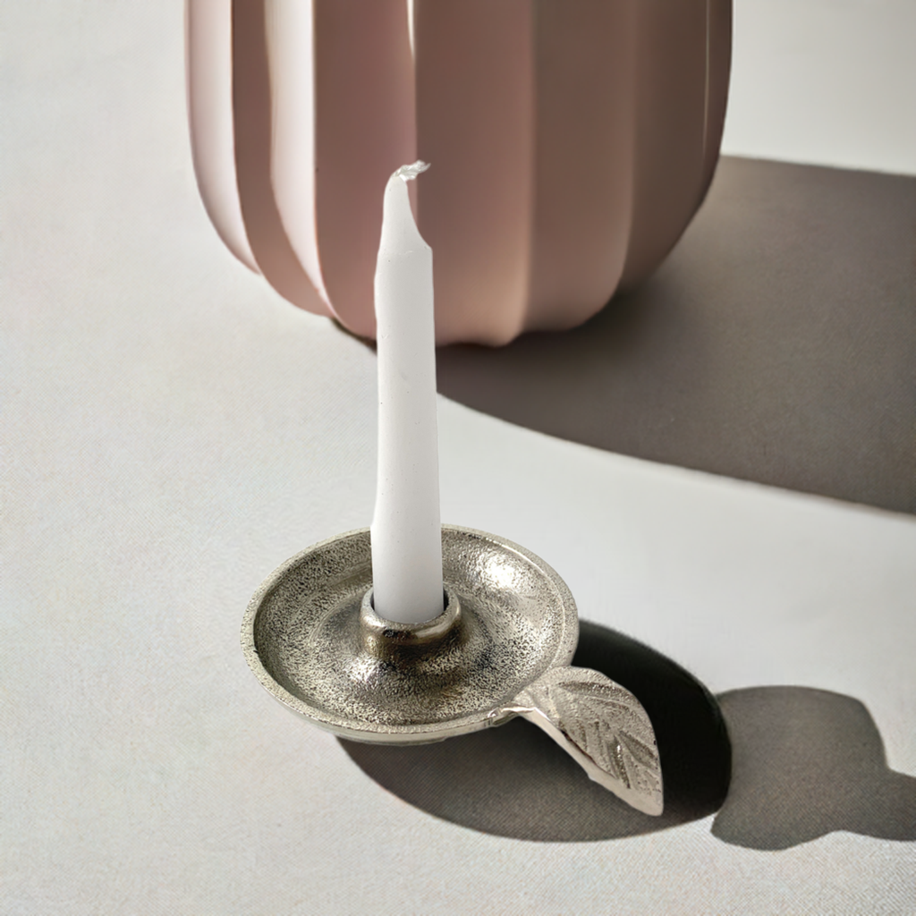 Silver leaf-handle taper candle holder with a white candle beside a blush vase